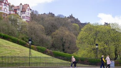 Springtime view of Edinburgh Castle from Princes Street with people walking and lush green trees.