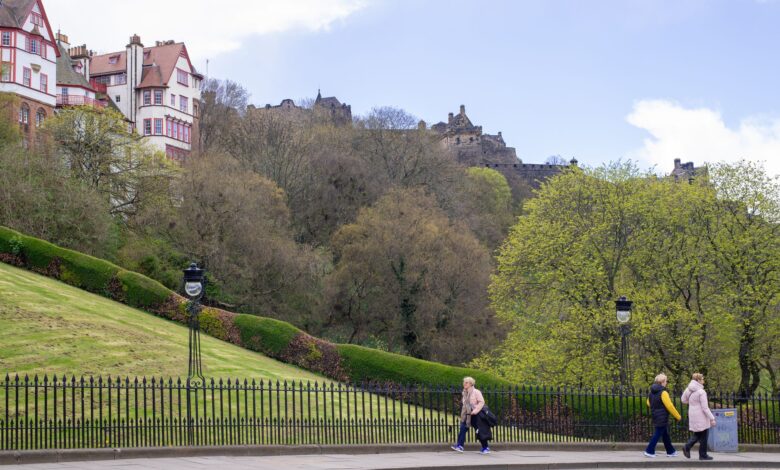 Springtime view of Edinburgh Castle from Princes Street with people walking and lush green trees.