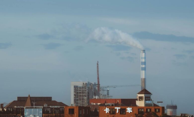 Factory with smokestack emitting smoke under a clear sky, industrial setting.
