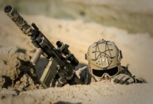 A soldier with tactical gear hiding in the desert, poised for action.