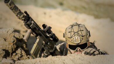 A soldier with tactical gear hiding in the desert, poised for action.