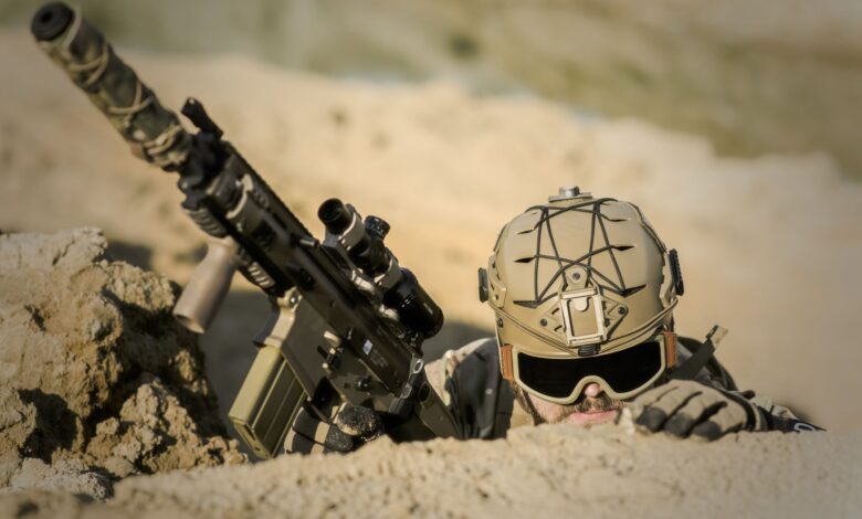 A soldier with tactical gear hiding in the desert, poised for action.