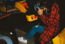 Young woman enjoying an arcade racing game wearing a checkered shirt. Fun and leisure activity captured indoors.