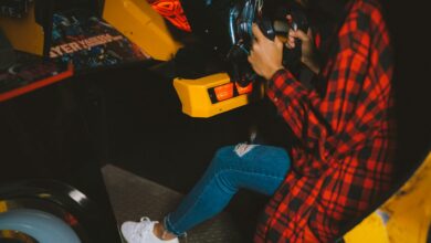 Young woman enjoying an arcade racing game wearing a checkered shirt. Fun and leisure activity captured indoors.