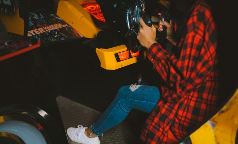 Young woman enjoying an arcade racing game wearing a checkered shirt. Fun and leisure activity captured indoors.