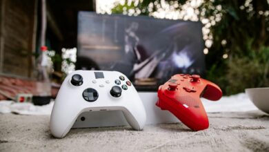 White and red Xbox wireless controllers set outdoors. A computer screen is blurred in the background.