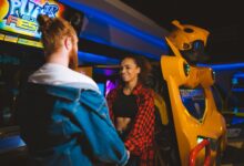 Happy couple holding hands and smiling in a vibrant arcade setting.
