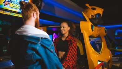 Happy couple holding hands and smiling in a vibrant arcade setting.