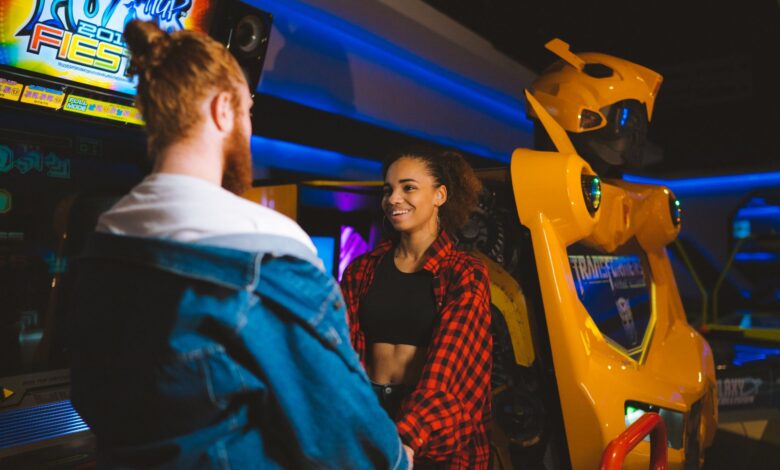Happy couple holding hands and smiling in a vibrant arcade setting.
