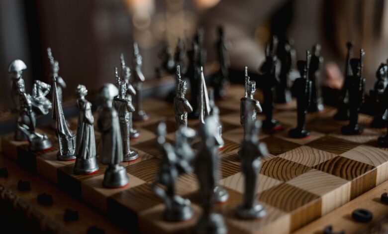 Detailed close-up of metallic chess pieces on a wooden board, showcasing a strategic game in progress.