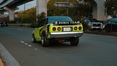 A vintage green car drives on an urban highway in Tokyo with distinct banners and decals.