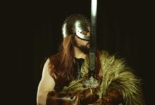A medieval warrior in full armor, wearing a helmet and holding a large sword.