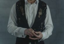 A person dressed in a steampunk vest shuffling a deck of cards indoors.