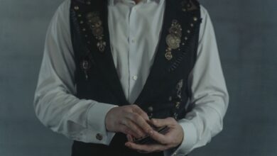 A person dressed in a steampunk vest shuffling a deck of cards indoors.