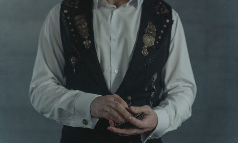 A person dressed in a steampunk vest shuffling a deck of cards indoors.
