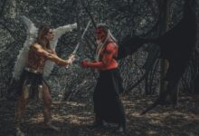 A dramatic cosplay scene of an angel and demon with swords in a forest.