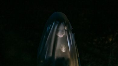 Mysterious little girl standing in darkness covered with white blanket as ghost and shining flashlight on face