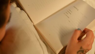 Close-up of a person reading a book indoors, showcasing a tattooed hand for a cozy and personal touch.