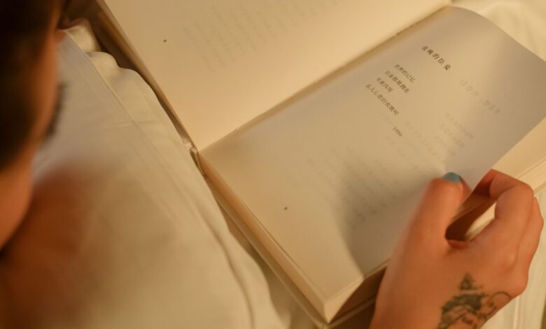 Close-up of a person reading a book indoors, showcasing a tattooed hand for a cozy and personal touch.