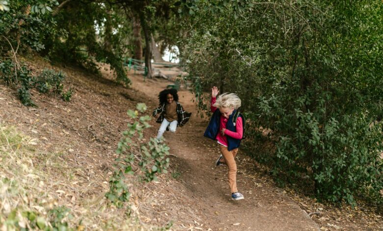 Two children joyfully running along a forest trail, surrounded by lush greenery.