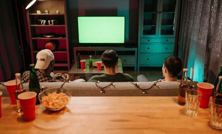 Three friends sitting on a couch playing video games together in a cozy living room setting.