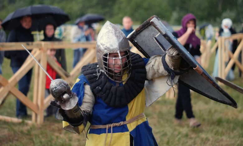 A knight in full armor engaged in a lively medieval reenactment outdoors.