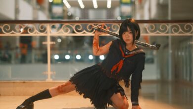 Cosplayer in dynamic pose with weapon in a modern indoor setting, showcasing intricate costume details.