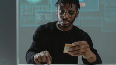 Man with glasses holding a bank card while typing on a keyboard, sitting in front of a computer.