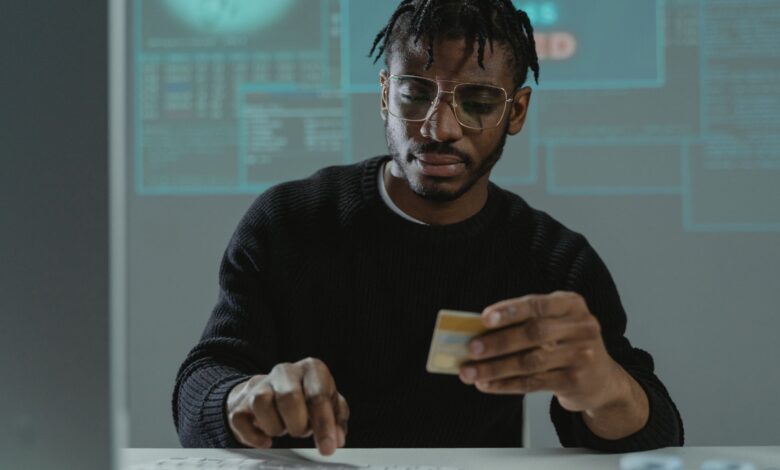 Man with glasses holding a bank card while typing on a keyboard, sitting in front of a computer.