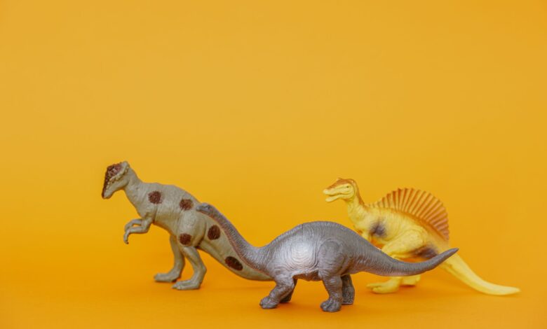 Three dinosaur toy figurines on a vibrant yellow background, ideal for playful concepts.