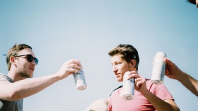 Group of young adults cheering with drinks under a clear blue sky.
