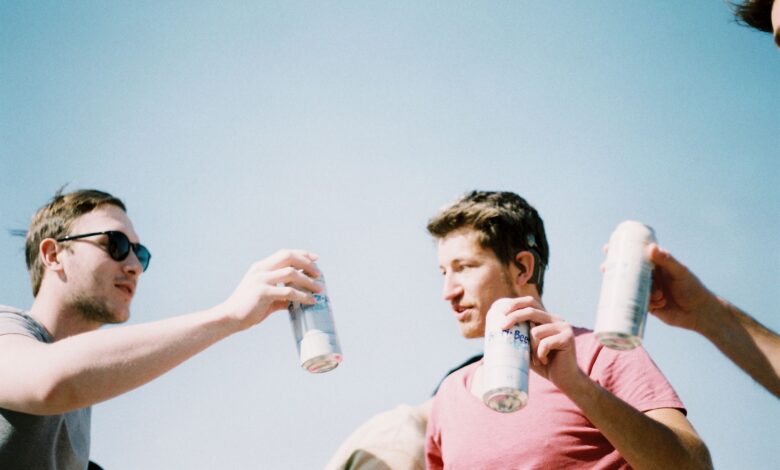 Group of young adults cheering with drinks under a clear blue sky.
