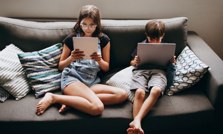 Two children engaging with tablets on a sofa, creating a modern lifestyle scene.
