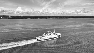 Black and white photo of Red Funnel ferry navigating the Solent with a coastal landscape in the background.
