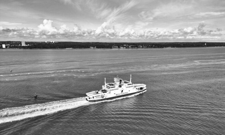Black and white photo of Red Funnel ferry navigating the Solent with a coastal landscape in the background.