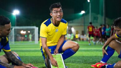 A soccer coach strategizing on a field with players during a night game session.