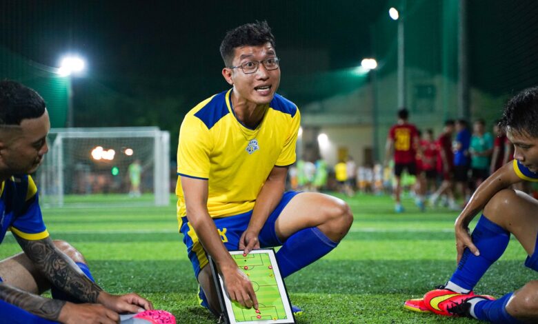 A soccer coach strategizing on a field with players during a night game session.