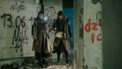 Two people exploring an abandoned, graffiti-filled building with flashlights, evoking a post-apocalyptic atmosphere.