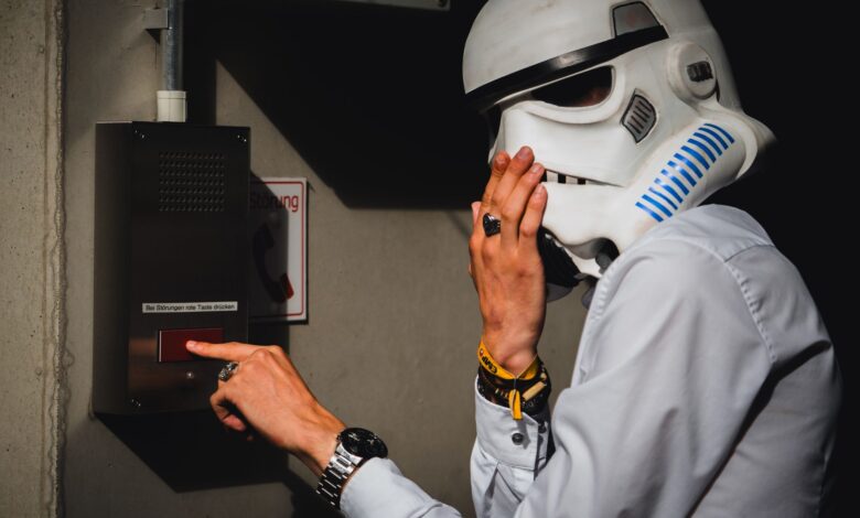 A person wearing a Stormtrooper helmet interacts with an intercom in an indoor setting.