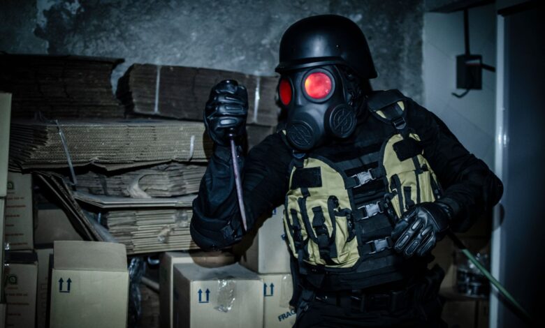 Individual in tactical gear and gas mask holding a weapon in an abandoned warehouse.