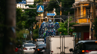 A large robot statue dominates the traffic scene in a bustling Bangkok street.