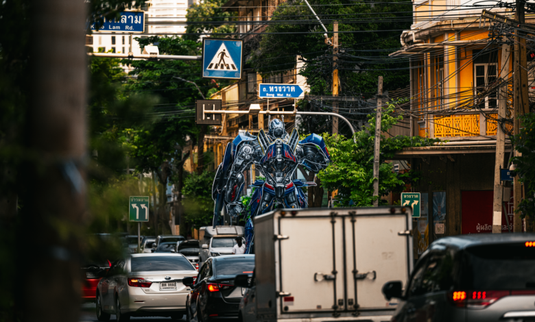 A large robot statue dominates the traffic scene in a bustling Bangkok street.