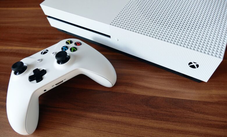 Close-up of a white Xbox console and controller on a wooden surface, ideal for gaming enthusiasts.