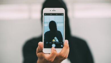 A person in a hoodie takes a mysterious selfie with a smartphone.