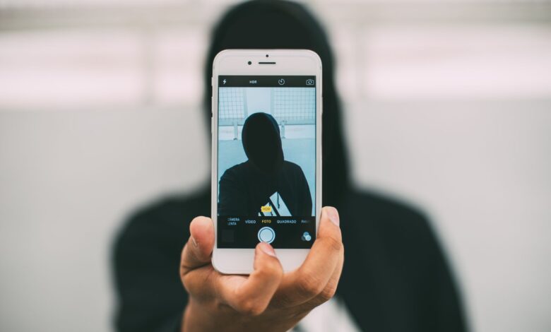 A person in a hoodie takes a mysterious selfie with a smartphone.