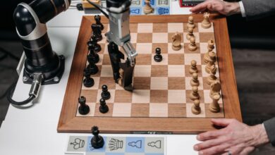 A robotic arm playing chess against a human hand on an electronic chessboard indoors.