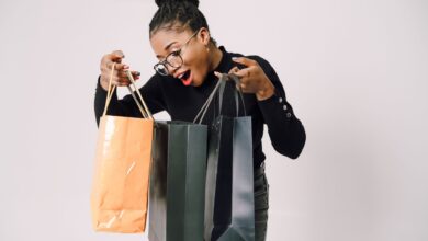 A smiling woman with eyeglasses happily admires her shopping bags against a white background.