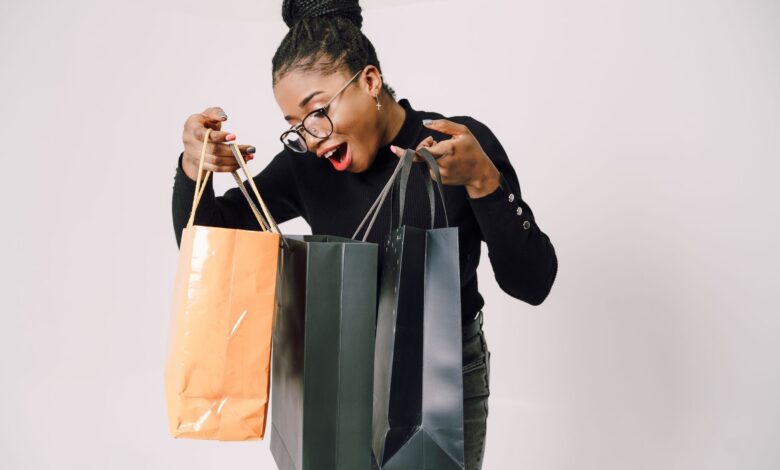 A smiling woman with eyeglasses happily admires her shopping bags against a white background.