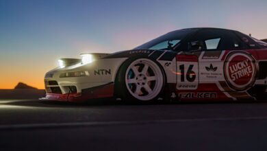 A sleek racing car with branded decals against a vibrant sunset backdrop on an open road.