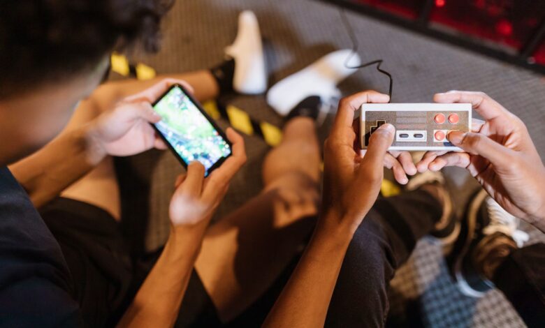 Close-up of teenagers playing mobile and retro video games indoors, showcasing fun and technology.
